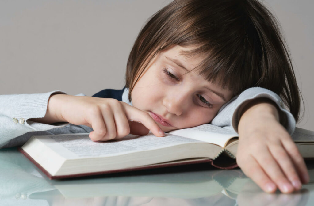 A young child girl lacks interest in reading, pointing her finger to the word she is reading with a sad face.