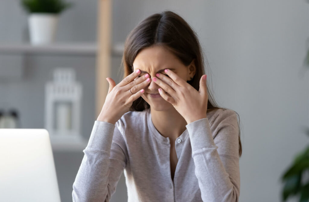 A young woman is rubbing her dry, irritable eyes, suffering from eye strain after a long hour working on her computer.