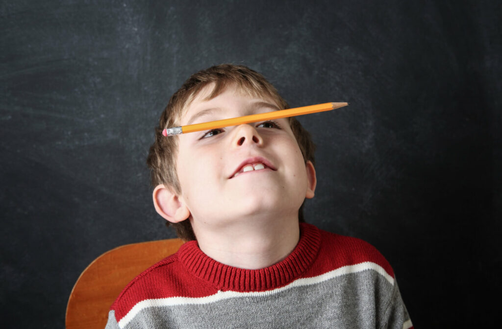 A child sitting on a chair balancing a pencil on his nose.
