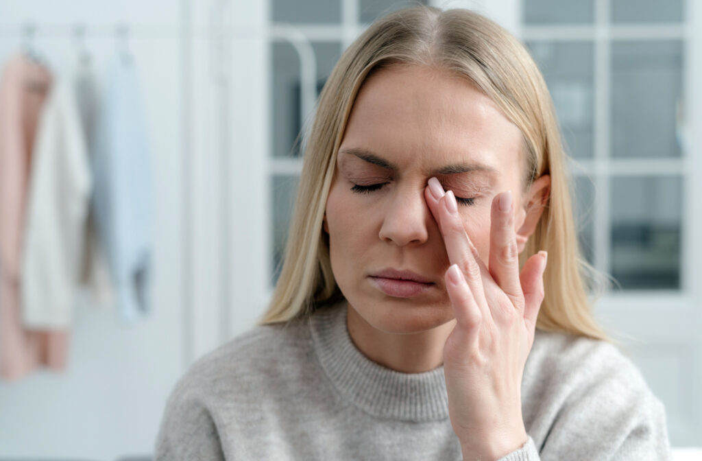 A woman experiencing dry eyes and light sensitivity with her eyes closes and one hand rubbing the corner of her eye.