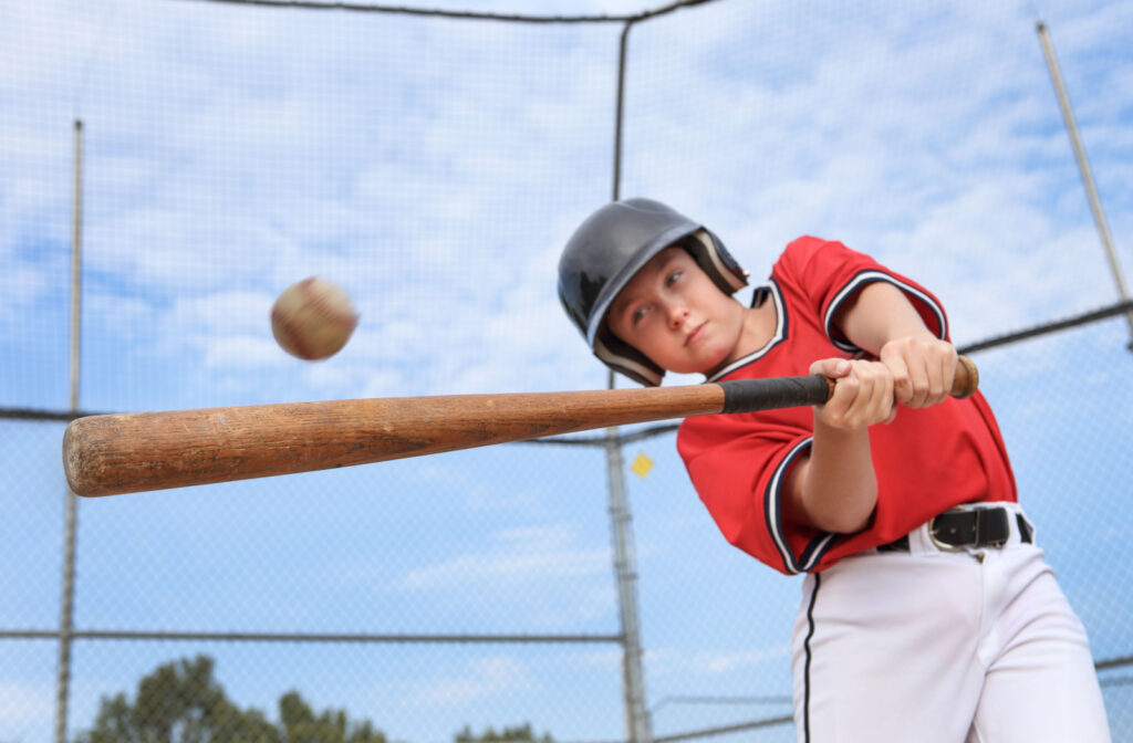 A baseball playing swinging the bat to hit the baseball with perfect timing thanks to sports vision therapy.