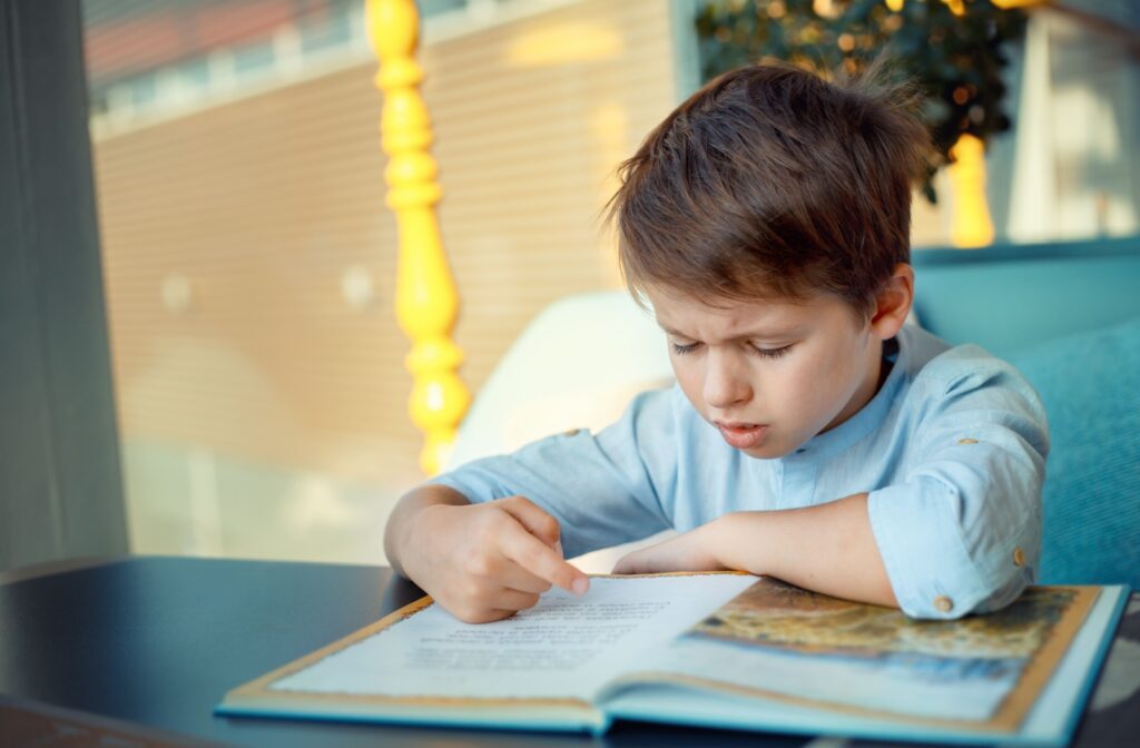 A young boy sitting at a table struggling to read due to vision problems.