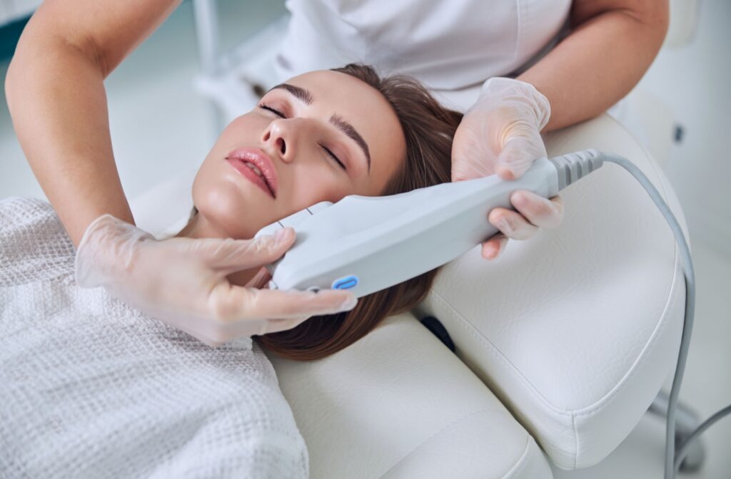 Dark haired person smiles while receiving a photofacial by a gloved professional.
