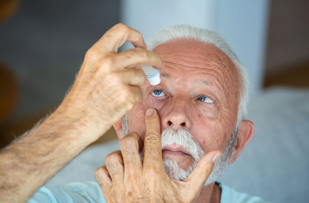 An older man pulls combats dry eye by pulling down the lid of his right eye and applying eye drops.