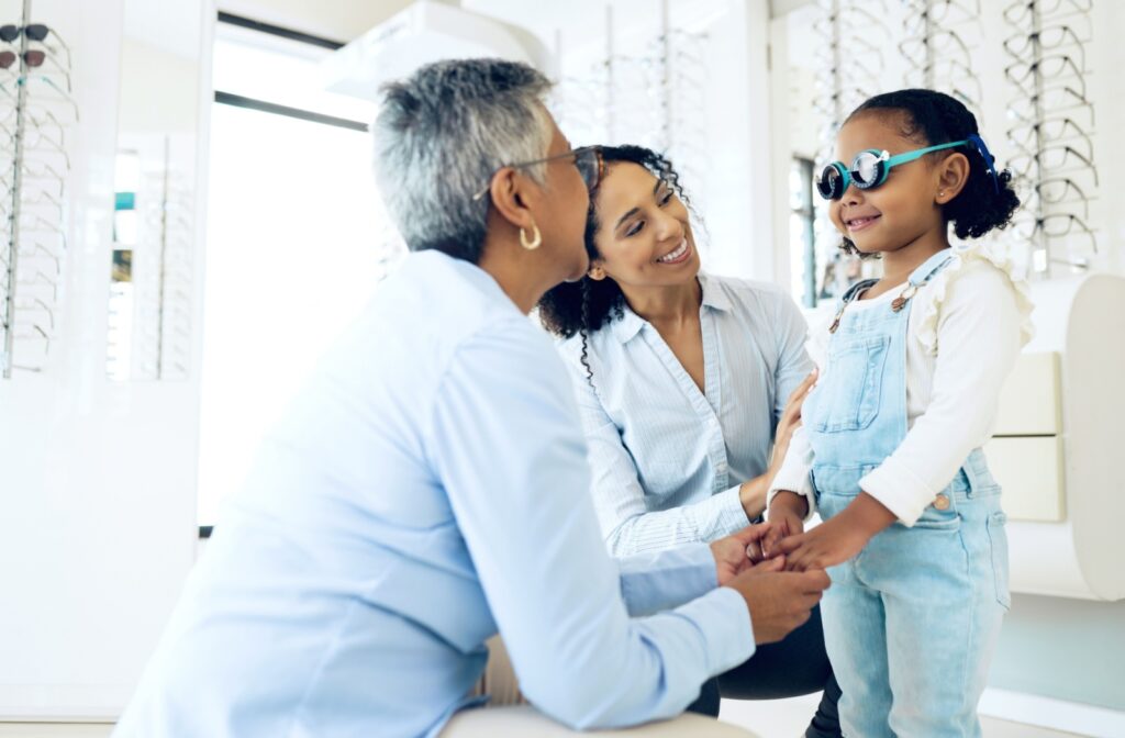 A child wearing vision therapy glasses smiles while receiving care from two supportive adults in an eye care clinic