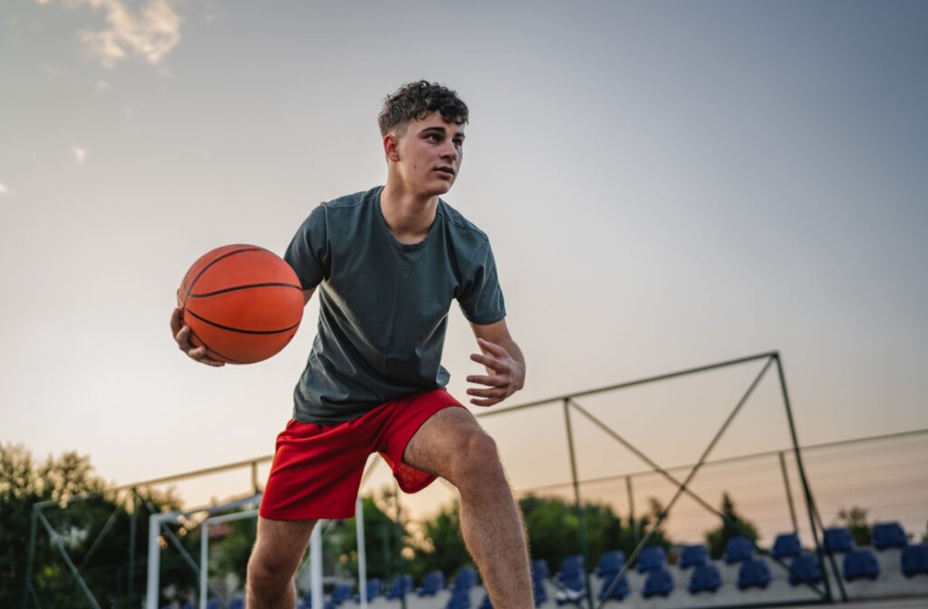 A young person dribbles a basketball on an outdoor court during practice.