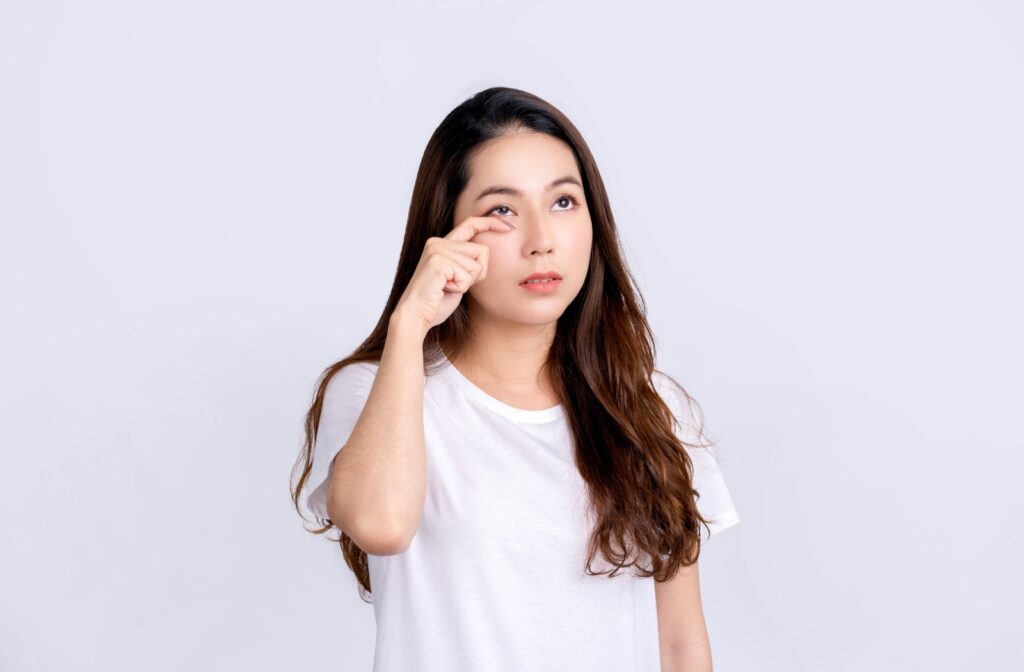 A woman in a white shirt rubs her eye while looking up
