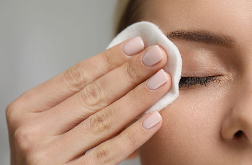 A close up of a hand wiping a cotton pad across the eye of someone who is wearing makeup