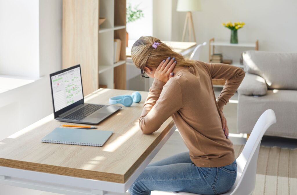 Woman sits at a desk and holds on to her lower back and neck