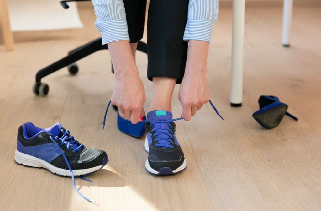Person switching their shoes from high heels to a pair of blue running shoes.