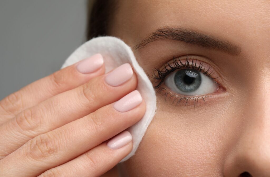 A close up of a person using a cotton pad to remove the makeup from their eye