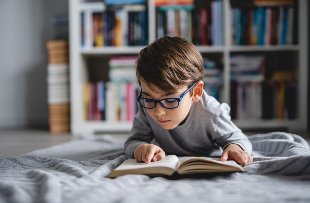 A young child reads a book while wearing glasses