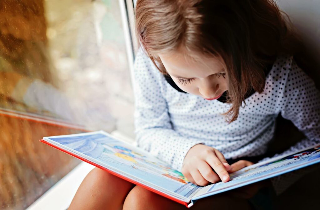 A child reading a book while sitting next to a window