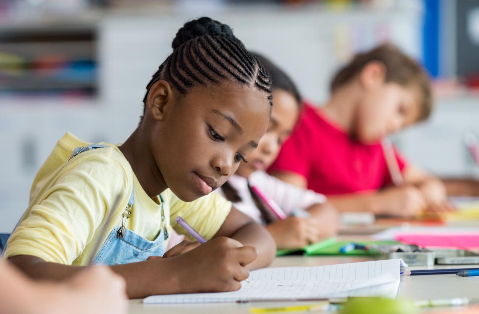 A young child writing in a notepad during school